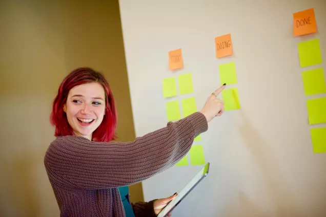 Photo of a happy person writing on a post it on a whiteboard.
