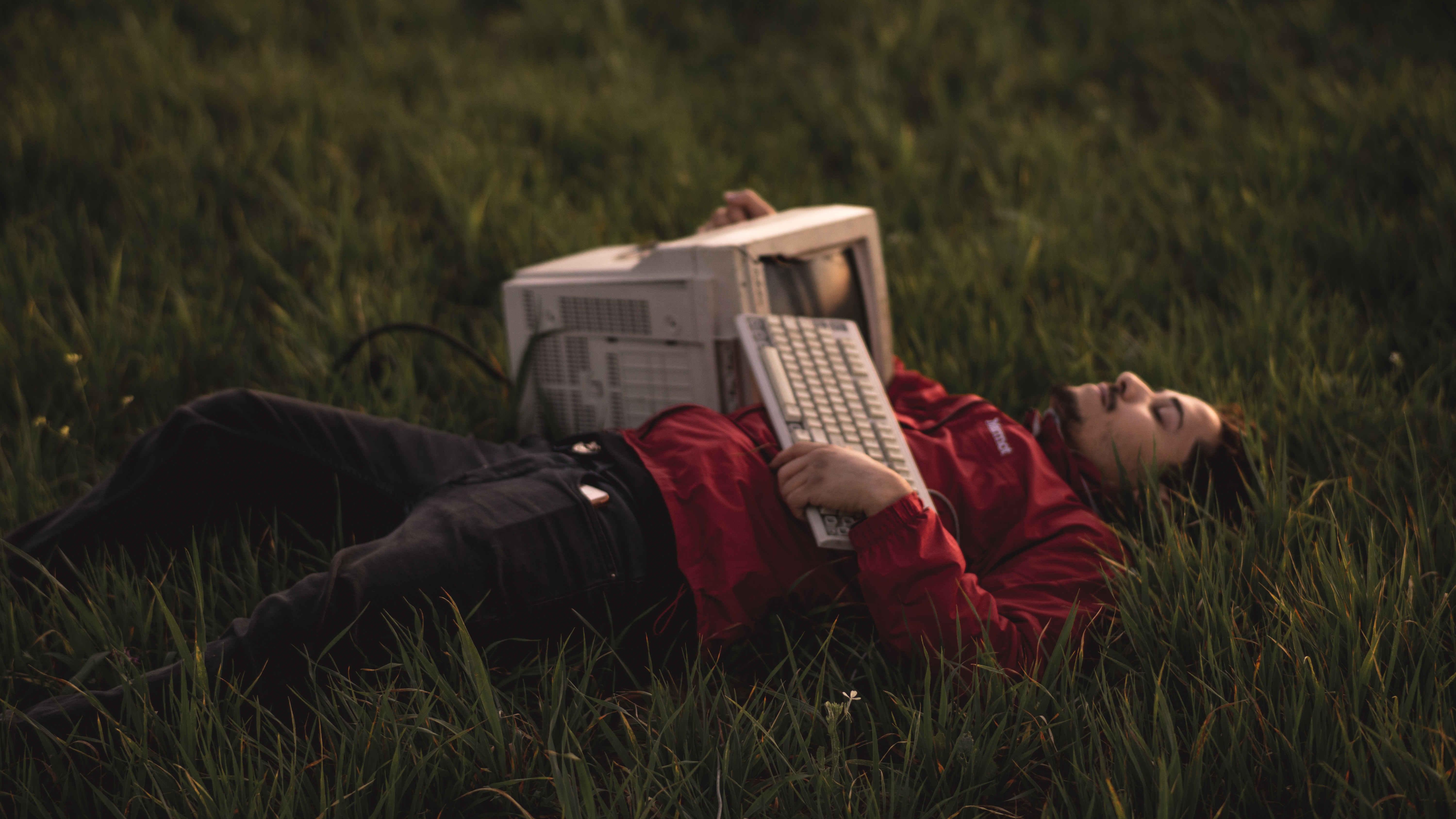 Foto som visar en person som ligger ner i gräset med en gammal stationär dator i famnen.