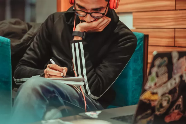 Foto med en student som sitter koncentrerad med hörlurar och skriver.