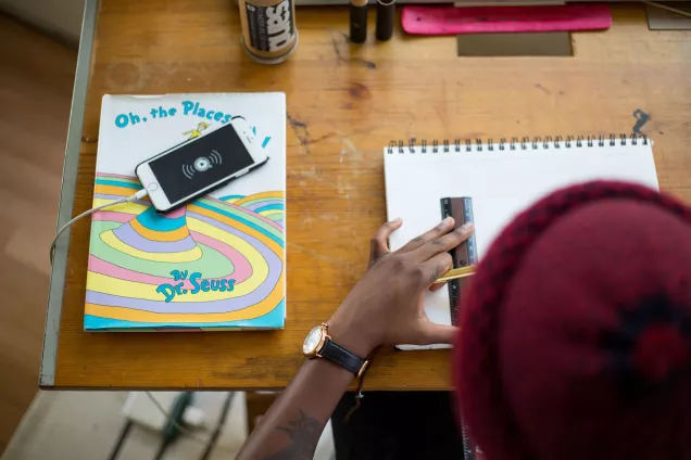 Foto på en student som sitter och arbetar vid ett skrivbord och har en mobil vid sidan av sig som ringer.